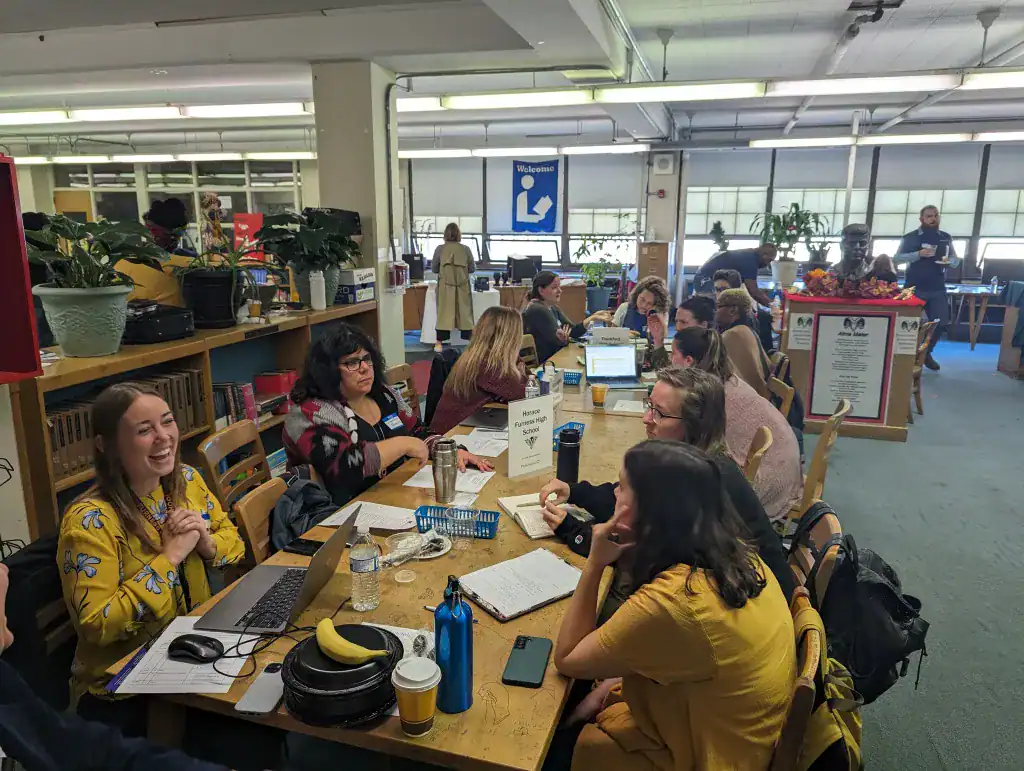 Adults sit at tables in a library to meet with each other as part of the 9th Grade Success Network.