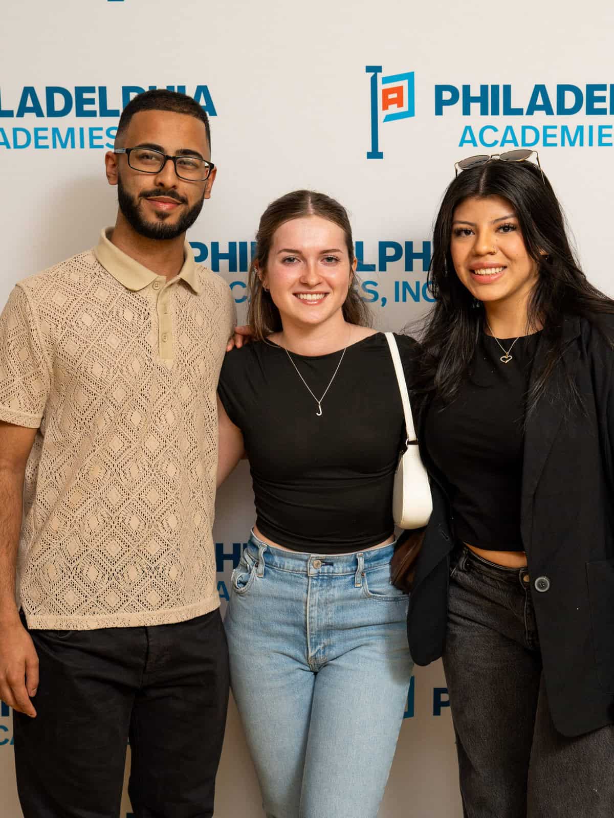 Three middle school students pose in front of a Philadelphia Academies step and repeat.
