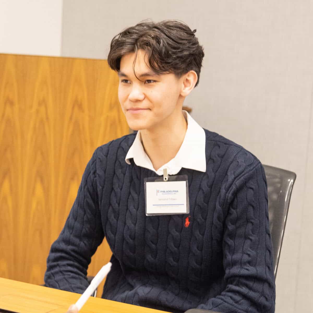 A student with a badge looks across the table with a smirk on his face.