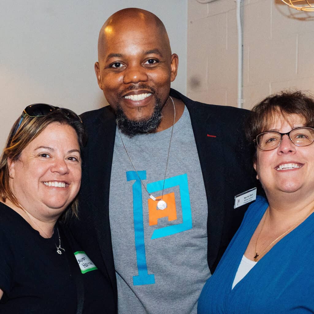 A woman on the left, a man in the middle with a Philadelphia Academies shirt, and a woman on the right are all smiling at the camera.