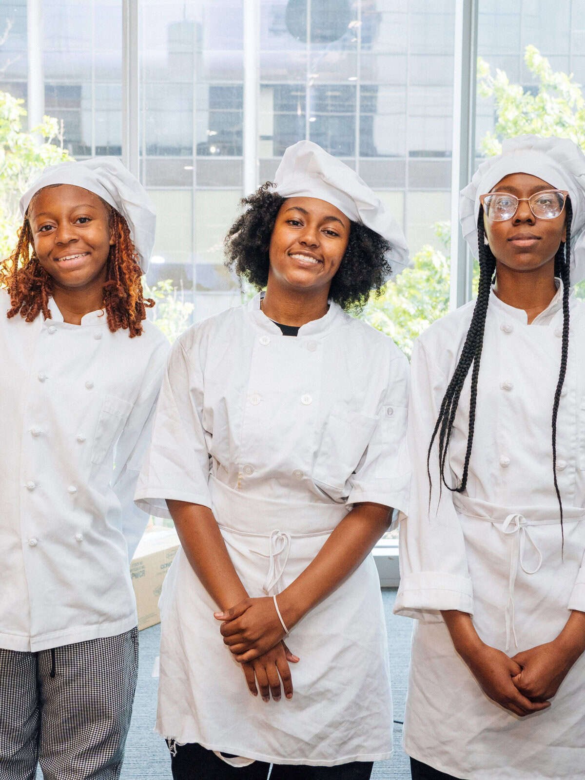 Three women pose for the camera wearing culinary attire as part of a workforce development program.